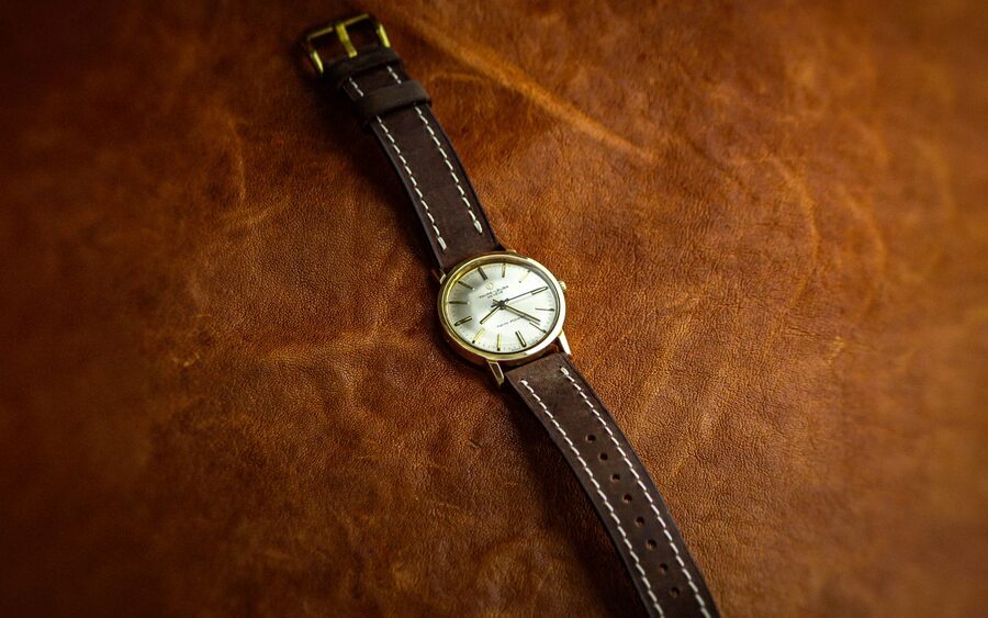 Montre à bracelet cuir marron avec surpiqûres claires posée sur une surface de cuir naturel, illustrant l'entretien à sec des bracelets en cuir