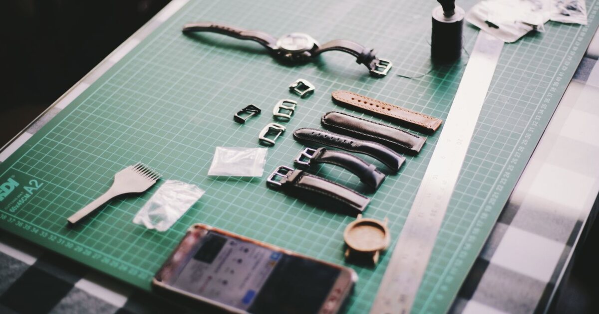 Plusieurs bracelets de montre en cuir alignés sur un tapis de découpe gradué à côté de boucles de rechange et d'un boîtier de montre nu, pour choisir la bonne largeur d'attache