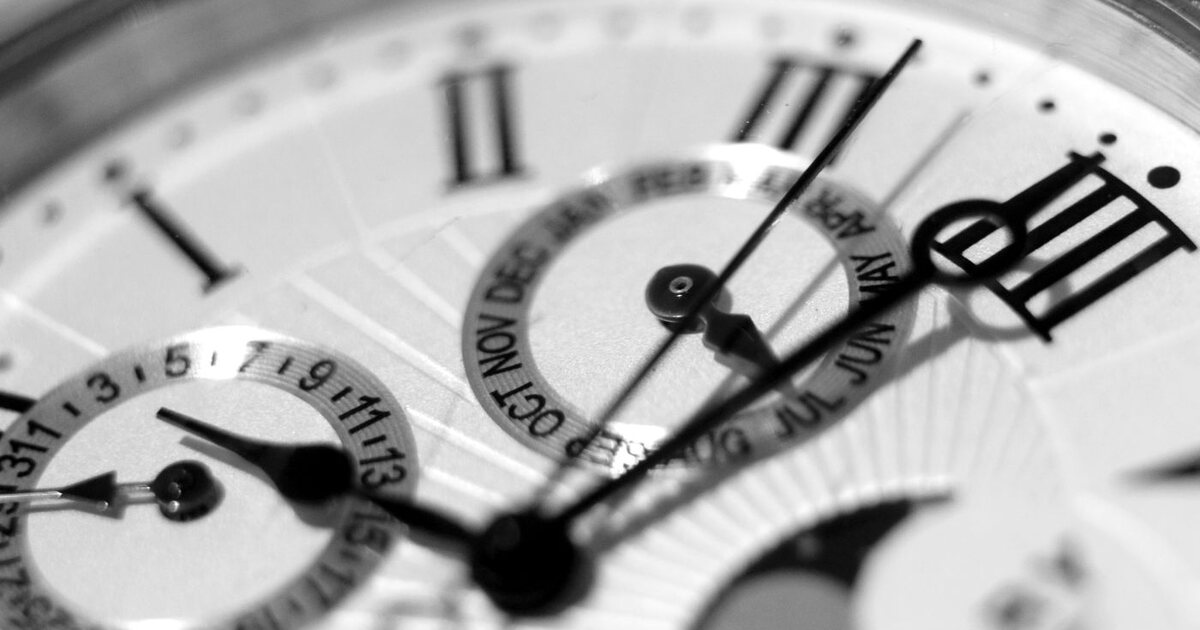 Macro en noir et blanc du cadran d'un chronographe montrant ses compteurs, ses aiguilles et son guichet de quantième