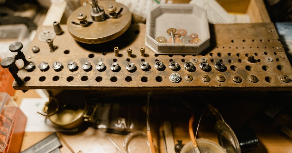 Établi d'horloger avec ses casiers de pièces détachées de montre, potence, bagues de réparation et outils de précision alignés sur le plan de travail d'un atelier horloger français
