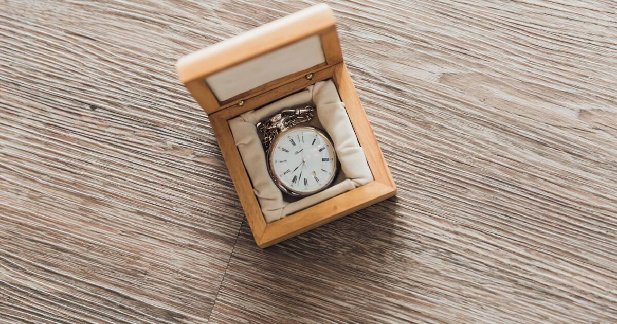 Montre à gousset ancienne présentée dans un écrin en bois ouvert, posée sur un parquet clair