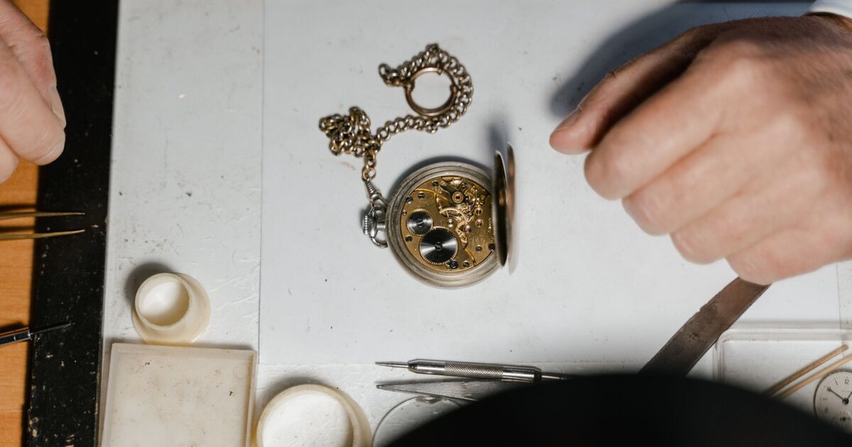 Montre à gousset ancienne en argent posée sur l'établi d'un horloger, fond ouvert laissant voir le mouvement mécanique doré, sa chaîne et les outils de rhabillage