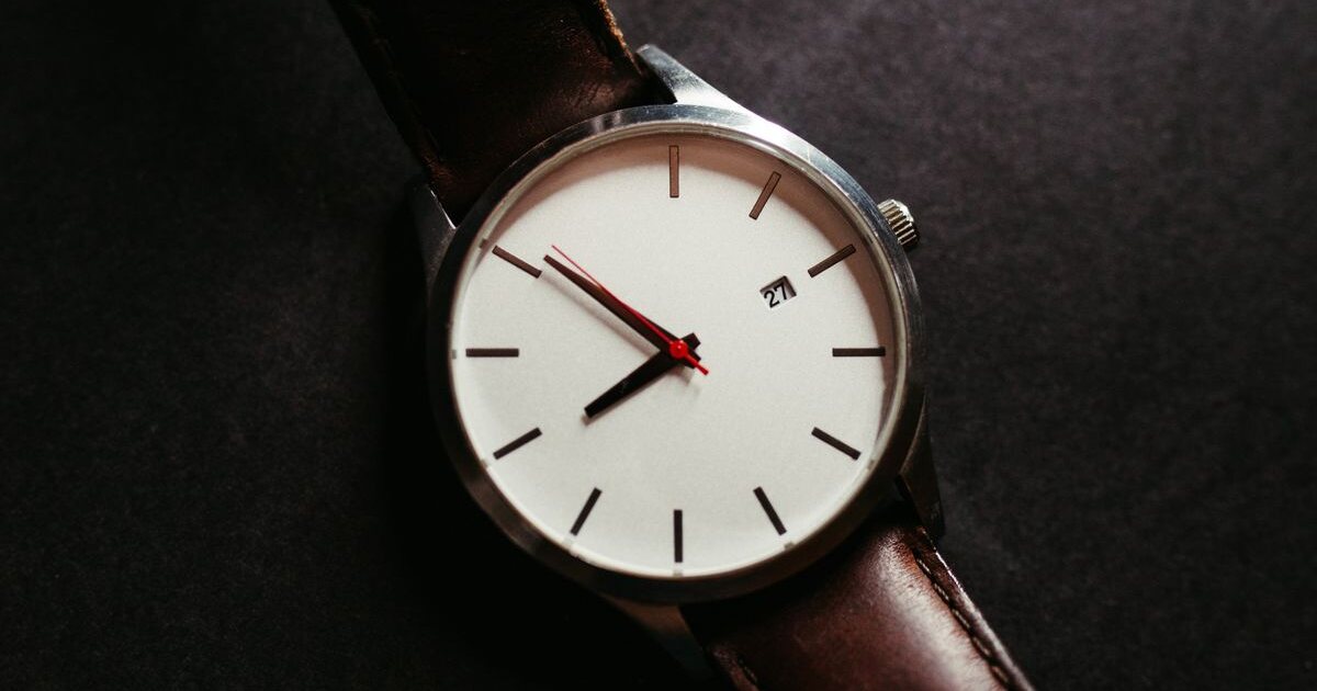 Montre minimaliste à cadran blanc et bracelet en cuir brun posée sur fond sombre, boîtier fin et index bâtons caractéristiques des montres de style Daniel Wellington