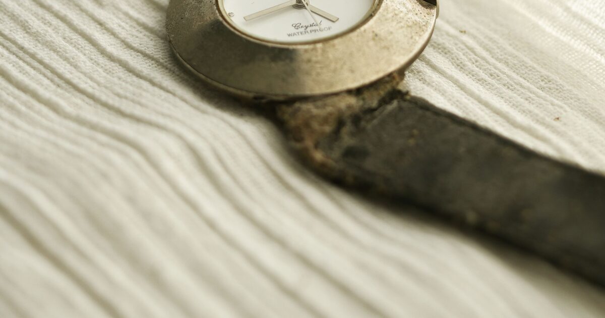 Montre ancienne au boîtier terni dont le bracelet en cuir est craquelé et décomposé, posée sur un tissu clair