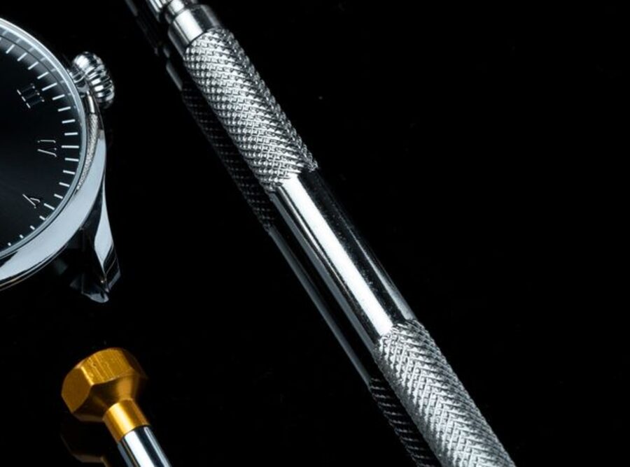 Outil à barrettes de précision posé près des cornes d'un boîtier de montre sans bracelet, sur fond noir