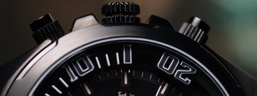 Gros plan sur les deux poussoirs de chronographe encadrant la couronne vissée d'une montre, vus de profil