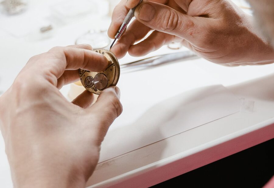 Horloger travaillant sur un mouvement de montre à l'établi avec un tournevis de précision, dans un atelier clair équipé pour le remplacement de verres