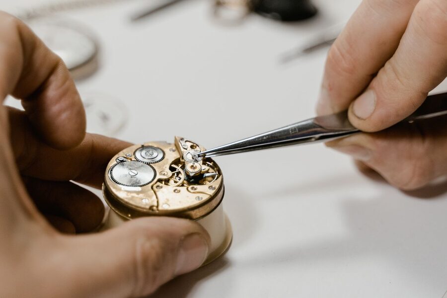 Horloger reposant une pièce à la brucelle sur un mouvement de montre mécanique démonté lors d'une révision en atelier