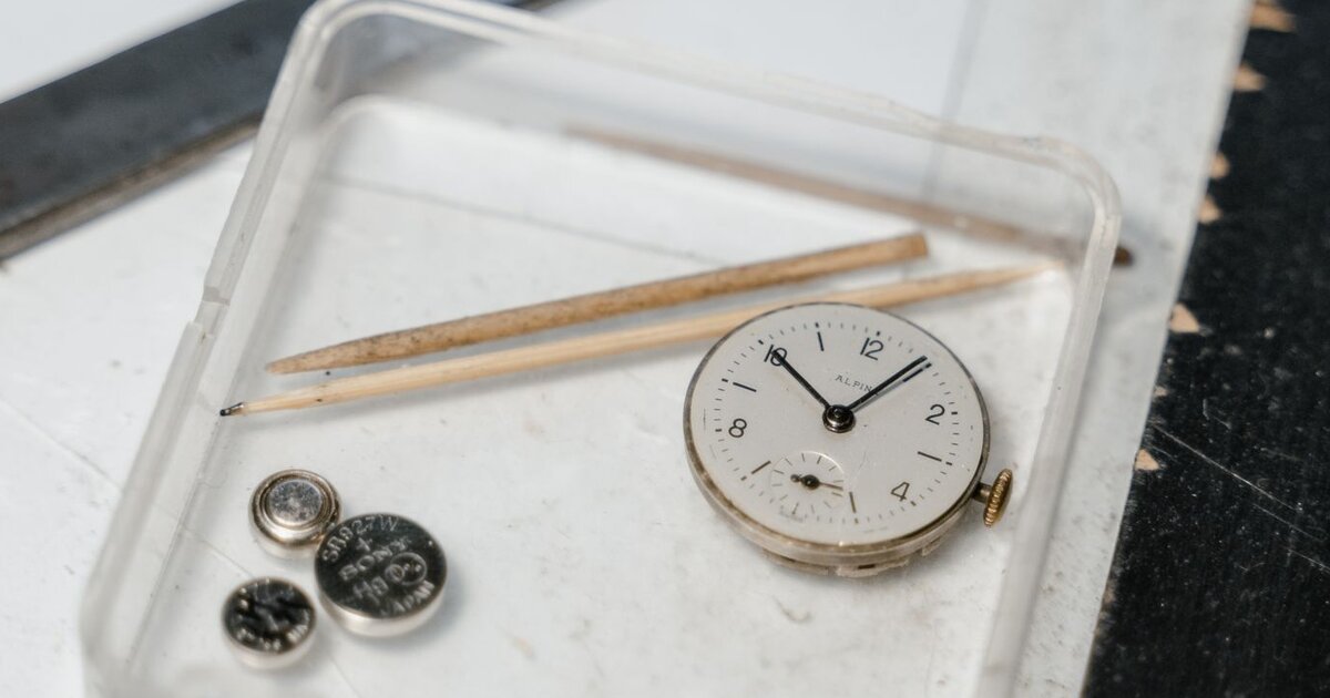 Mouvement de montre sorti de son boîtier posé près de piles bouton sur un plateau d'horloger