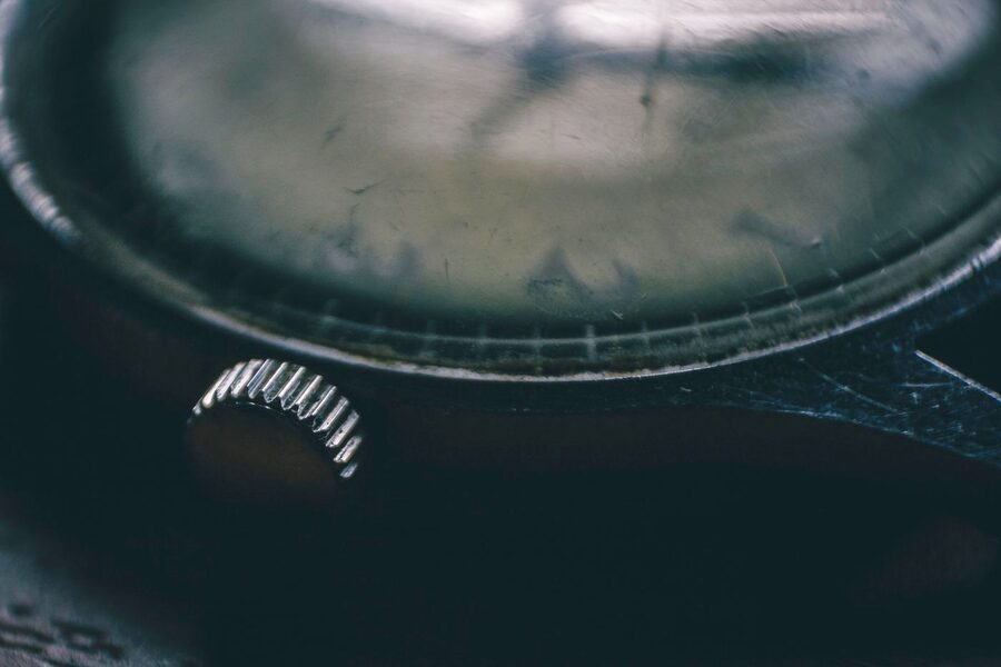 Profil du verre bombé d'une montre vintage posé sur la carrure du boîtier, sa tranche et ses rayures de surface visibles de côté